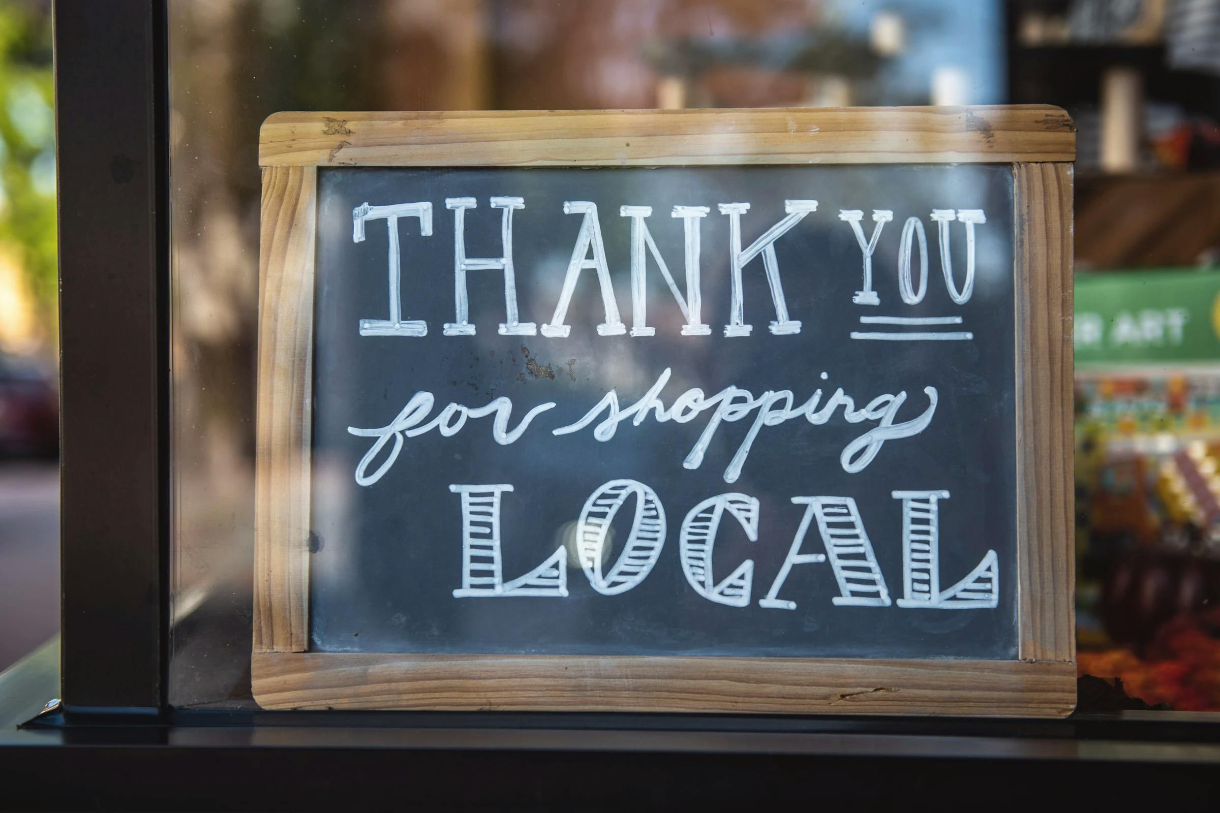 A sign in a shop window that reads "Thank you for shopping local"